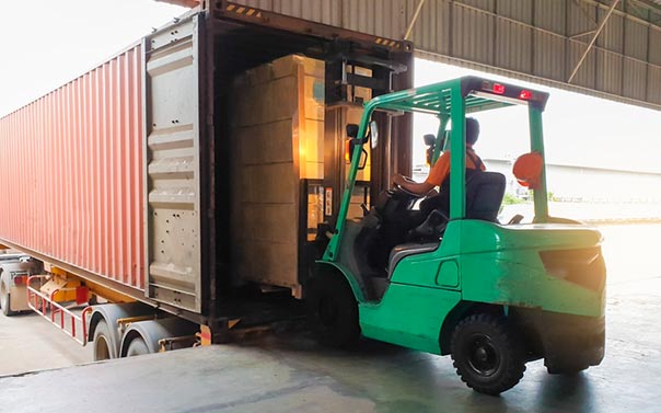 green forklift carries cargo boxes inside cargo truck